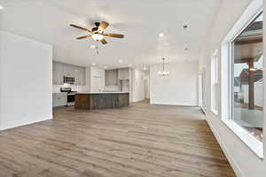 Unfurnished living room featuring sink, ceiling fan with notable chandelier, a textured ceiling, and light hardwood / wood-style flooring