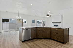 Kitchen featuring decorative light fixtures, dishwasher, an island with sink, sink, and light wood-type flooring