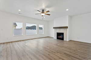 Unfurnished living room with a textured ceiling, a fireplace, light hardwood / wood-style floors, and ceiling fan