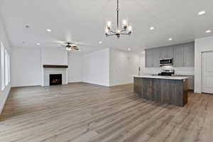 Kitchen with light hardwood / wood-style flooring, appliances with stainless steel finishes, gray cabinetry, a center island with sink, and decorative light fixtures