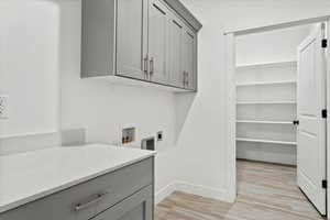 Clothes washing area featuring electric dryer hookup, hookup for a washing machine, light hardwood / wood-style flooring, and cabinets