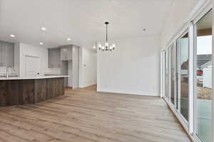 Kitchen featuring sink, an inviting chandelier, hanging light fixtures, gray cabinets, and light hardwood / wood-style floors