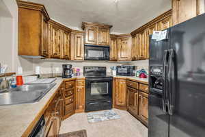 Kitchen with light tile patterned floors, sink, a textured ceiling, and black appliances