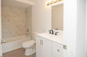 Full bathroom with vanity, hardwood / wood-style flooring, toilet, and tiled shower / bath combo