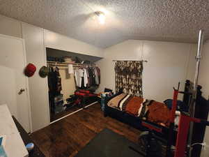 Bedroom with wood-type flooring, a closet, a textured ceiling, and vaulted ceiling