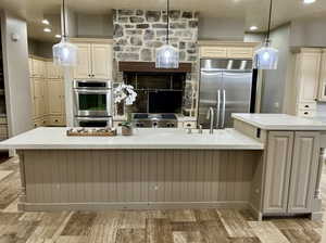 Kitchen featuring appliances with stainless steel finishes, pendant lighting, a center island with sink, and cream cabinetry