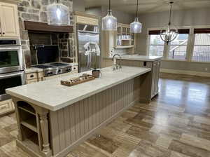 Kitchen with stainless steel appliances, decorative light fixtures, a center island with sink, and cream cabinetry