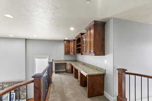 Interior space with light stone counters, light colored carpet, built in desk, and a textured ceiling