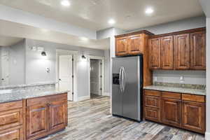 Kitchen featuring light stone counters, stainless steel fridge with ice dispenser, and light hardwood / wood-style flooring