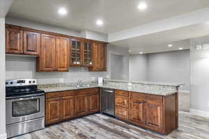 Kitchen featuring sink, stainless steel appliances, wood-type flooring, light stone countertops, and kitchen peninsula