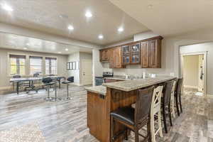 Kitchen with stainless steel electric range oven, a kitchen bar, kitchen peninsula, light stone countertops, and light wood-type flooring