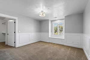 Empty room featuring a textured ceiling, a chandelier, and carpet flooring