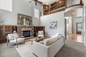 Living room with ceiling fan, a stone fireplace, hardwood / wood-style floors, and a towering ceiling