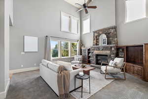 Carpeted living room with a stone fireplace, a towering ceiling, and ceiling fan