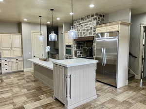 Kitchen featuring cream cabinets, decorative light fixtures, built in fridge, and an island with sink