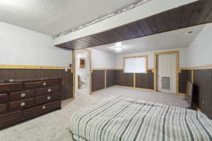 Carpeted bedroom with wooden walls, a textured ceiling, and ensuite bathroom