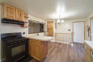 Kitchen with black gas range, hardwood / wood-style floors, an inviting chandelier, decorative light fixtures, and kitchen peninsula