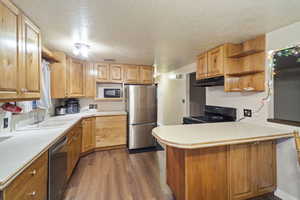 Kitchen with sink, dark wood-type flooring, black appliances, a textured ceiling, and kitchen peninsula