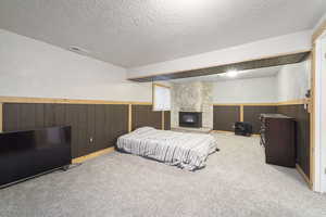 Bedroom featuring carpet floors, a fireplace, wooden walls, and a textured ceiling