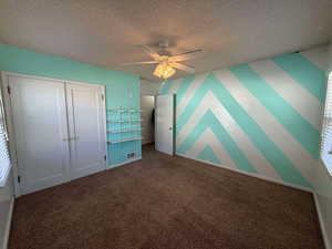 Unfurnished bedroom with ceiling fan, carpet floors, a closet, and a textured ceiling