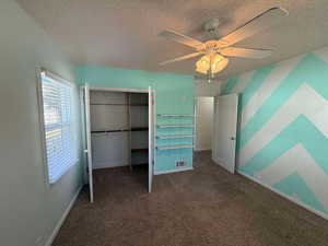 Unfurnished bedroom with a textured ceiling, a closet, ceiling fan, and dark colored carpet