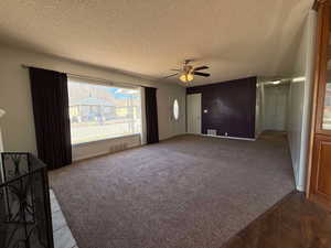 Unfurnished living room featuring ceiling fan, dark carpet, and a textured ceiling