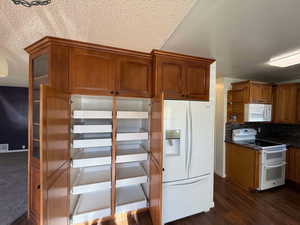 Kitchen with a textured ceiling, dark hardwood / wood-style flooring, white appliances, dark stone counters, and backsplash