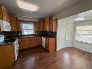 Kitchen featuring sink, white appliances, dark wood-type flooring, a skylight, and tasteful backsplash