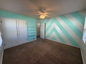 Unfurnished bedroom with ceiling fan, carpet flooring, a closet, and a textured ceiling