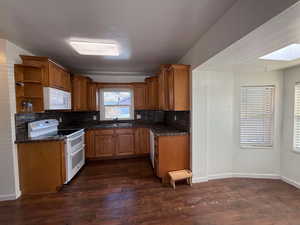 Kitchen with dark wood-type flooring, sink, a skylight, white appliances, and decorative backsplash