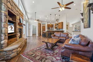 Living room featuring ceiling fan, high vaulted ceiling, a stone fireplace, and dark hardwood / wood-style flooring