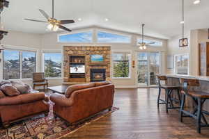 Living room with a stone fireplace, dark wood-type flooring, ceiling fan, and plenty of natural light