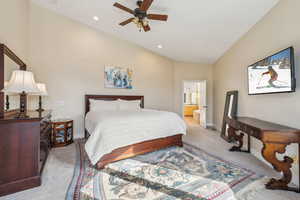 Carpeted bedroom featuring lofted ceiling, connected bathroom, and ceiling fan