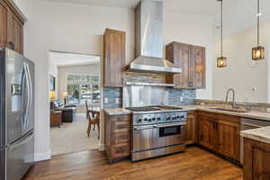 Kitchen featuring sink, backsplash, hanging light fixtures, stainless steel appliances, and wall chimney exhaust hood