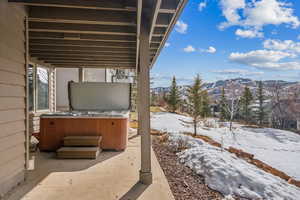 Snow covered patio with a hot tub and a mountain view