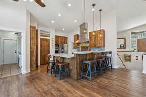 Kitchen featuring wall chimney exhaust hood, a kitchen bar, kitchen peninsula, pendant lighting, and stainless steel appliances