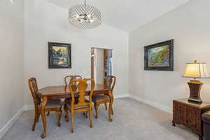 Dining room featuring an inviting chandelier, light colored carpet, and lofted ceiling