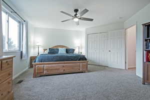 Bedroom with ceiling fan, light colored carpet, and a closet