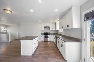 Kitchen featuring dark wood-type flooring, a breakfast bar area, appliances with stainless steel finishes, white cabinets, and decorative light fixtures