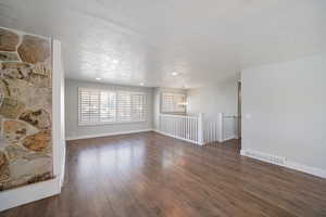 Empty room featuring dark hardwood / wood-style floors, a textured ceiling, and a notable chandelier