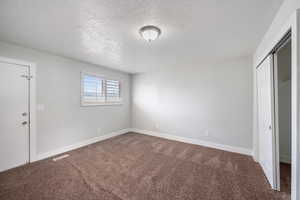 Unfurnished bedroom featuring dark colored carpet, a textured ceiling, and a closet