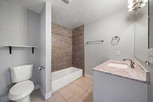 Full bathroom with tile patterned flooring, vanity, tiled shower / bath combo, toilet, and a textured ceiling