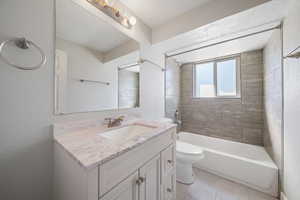 Full bathroom featuring vanity, tiled shower / bath combo, tile patterned floors, and toilet