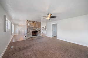 Unfurnished living room featuring ceiling fan with notable chandelier, a fireplace, carpet floors, and a textured ceiling