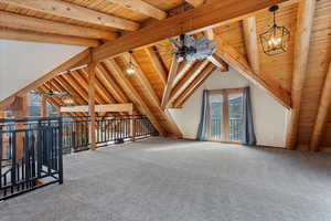 Bonus room featuring lofted ceiling with beams, wood ceiling, ceiling fan with notable chandelier, and carpet