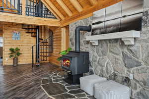 Interior space featuring dark wood-type flooring, wooden ceiling, a wood stove, wooden walls, and beamed ceiling