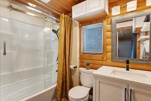 Full bathroom with wooden walls, vanity, wood ceiling, toilet, and shower / bath combo