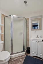 Bathroom featuring wood-type flooring, toilet, a shower with door, and vanity