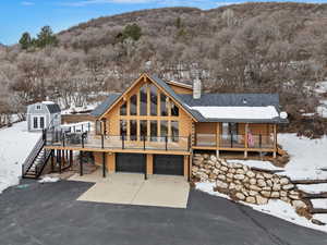 Snow covered property with a wooden deck, a garage, and an outdoor structure