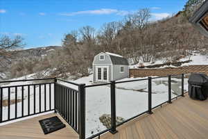 Snow covered deck featuring grilling area, an outdoor structure, and a mountain view